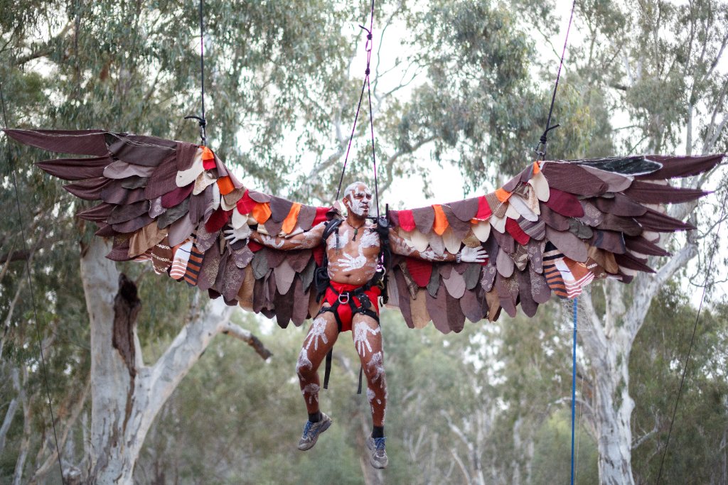 Indigenous performer suspended in flight with handcrafted wings and white ochre body paint