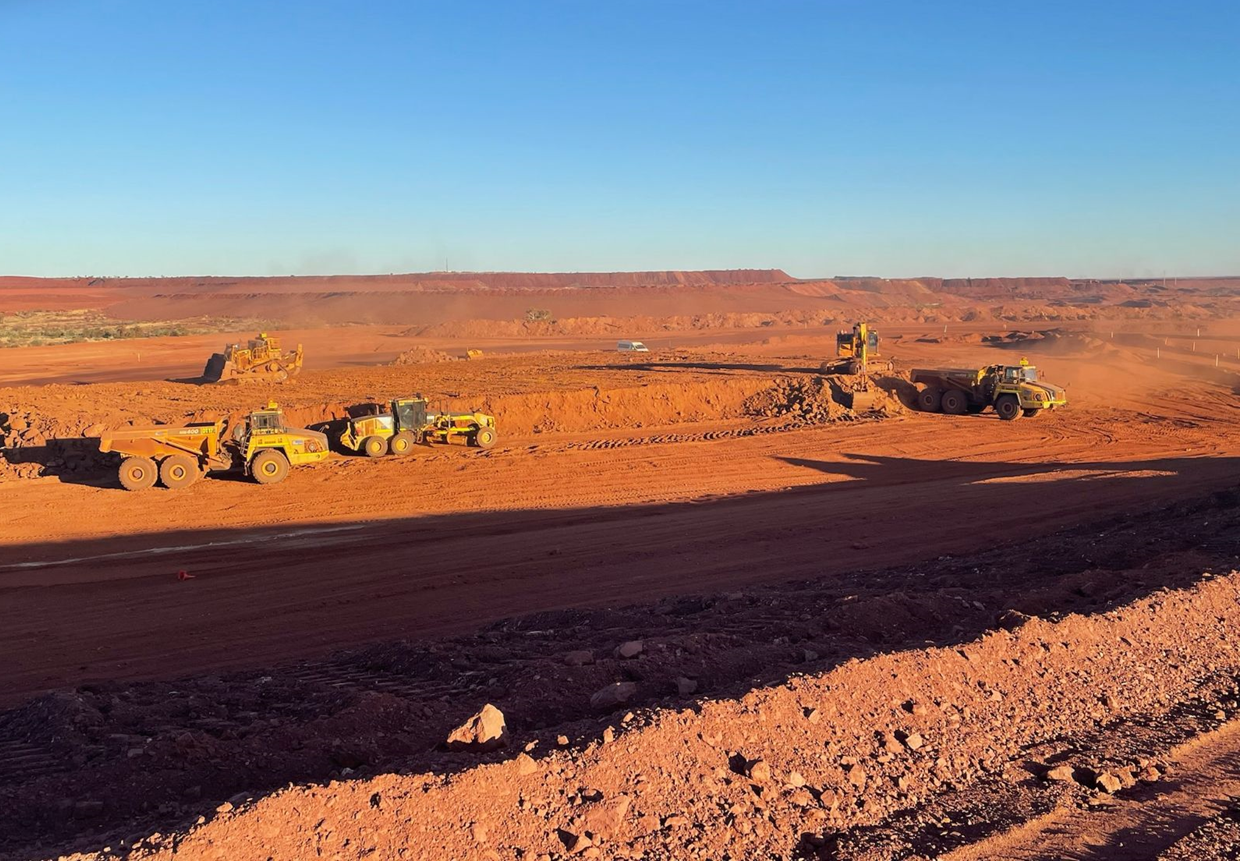 Open-pit mine site with GUMA dump trucks, grader and excavator working red earth