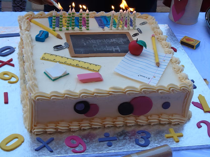 A colorful school-themed birthday cake with lit candles