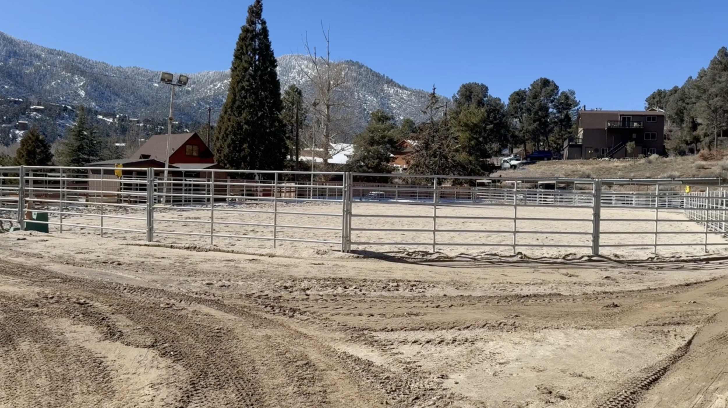 Outdoor equestrian riding arena with a snow-dusted mountain peak behind it near Frazier Mountain