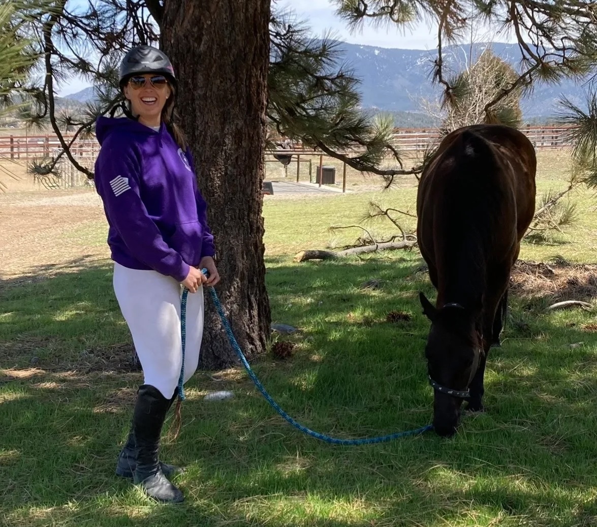 Sophia, horse trainer and nerve-release equine body worker, standing with a horse in a mountain pasture