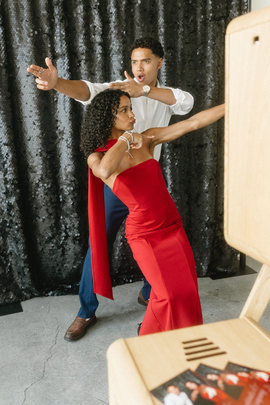 A couple posing playfully at a photo booth with a black sequin backdrop