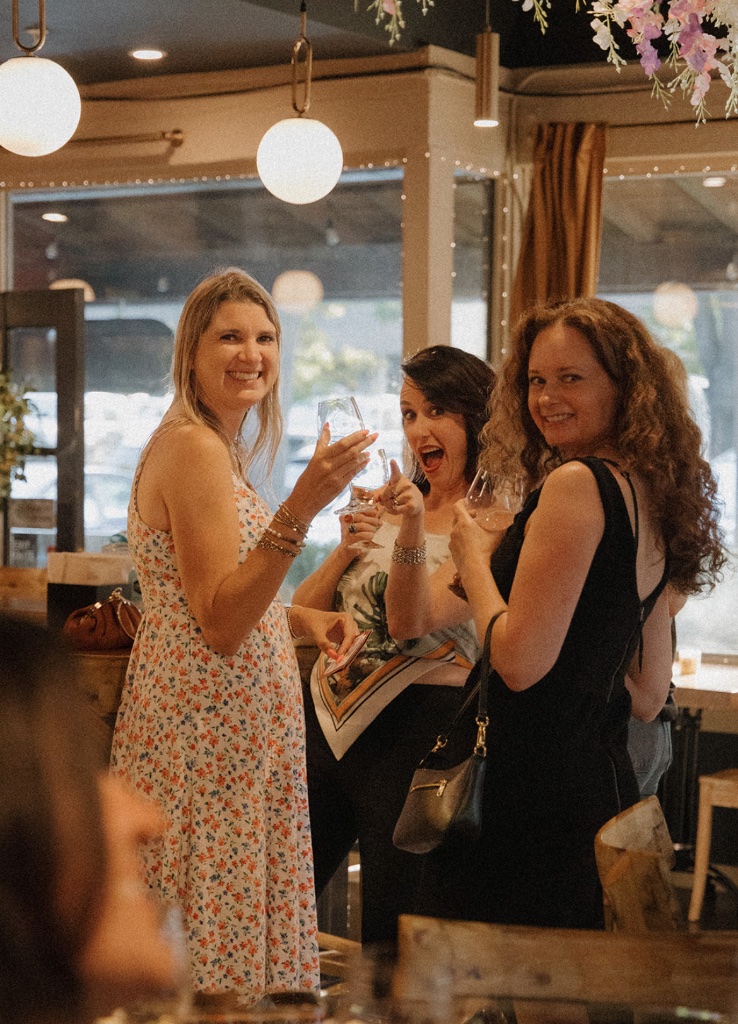 Three women laughing together with wine glasses at a social event