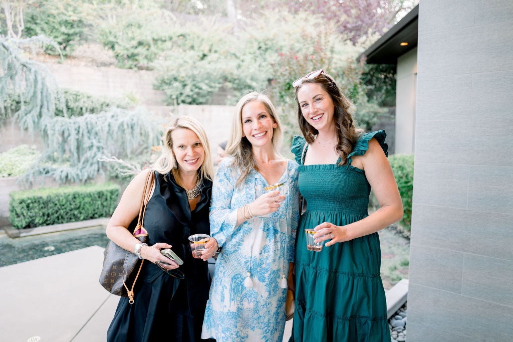 Three friends smiling together at an outdoor gathering