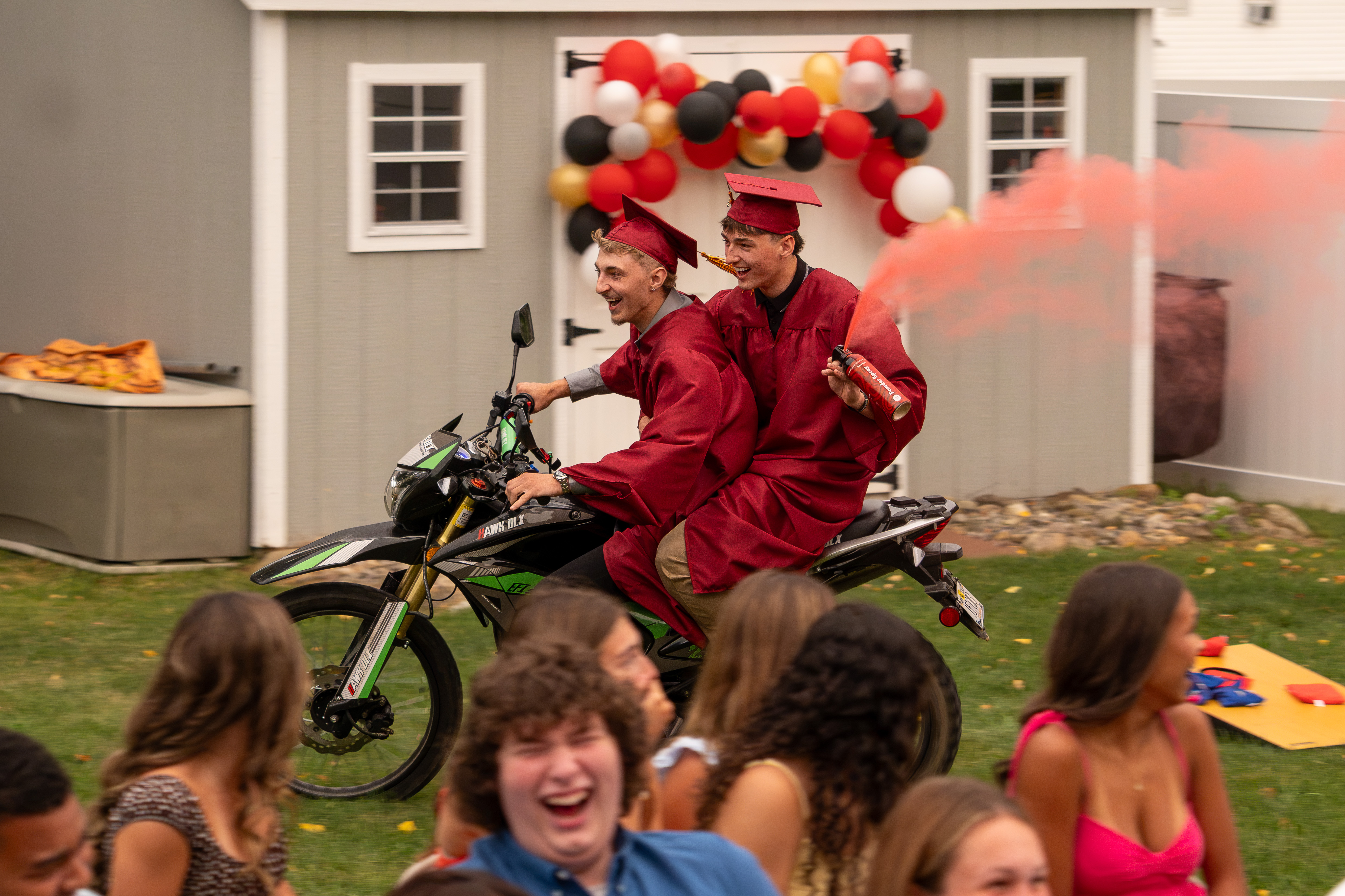 Aiden & Brady riding a motorcycle with a red smoke canister at their OC Grad Party