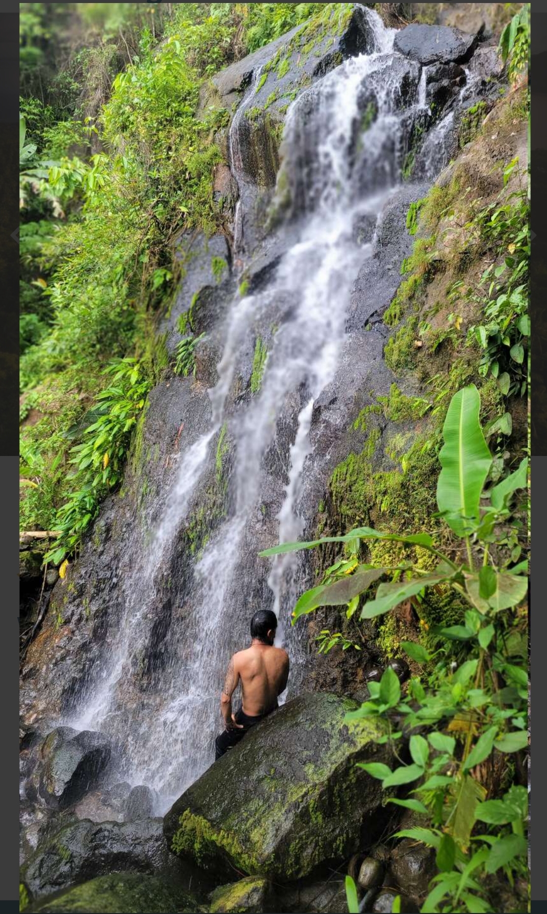 Guest resting on a moss-covered rock at the base of a tropical waterfall