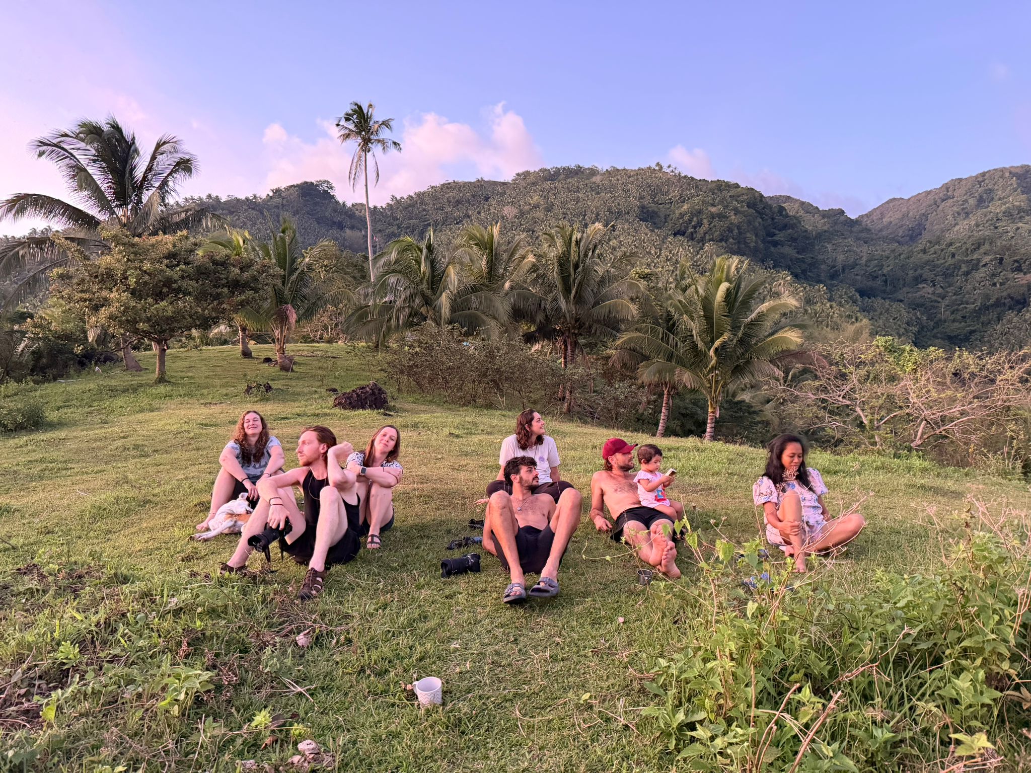 Group of friends and family sitting together on a grassy hillside at golden hour