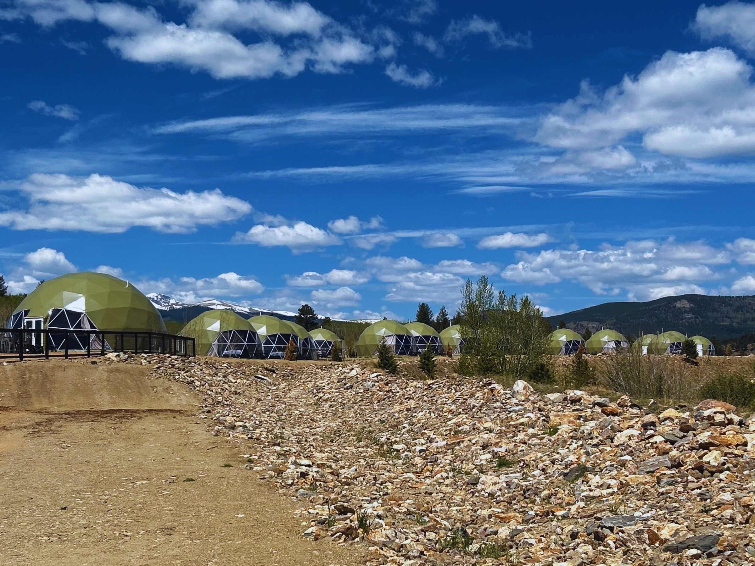 Row of green geodesic domes with snow-capped peaks beyond
