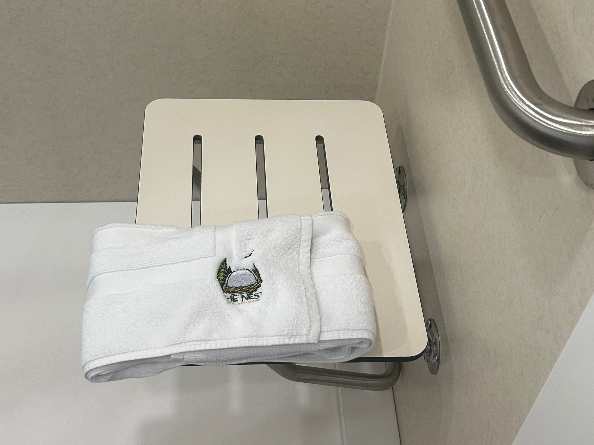 Fold-down accessible shower seat with branded The Nest towel