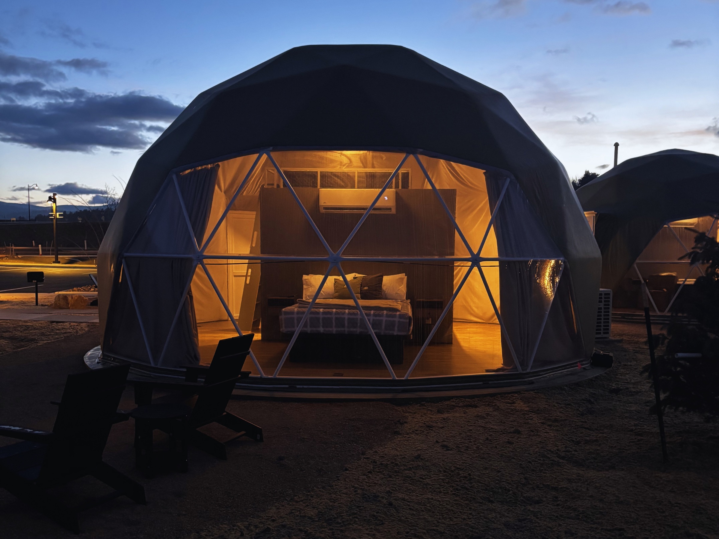 Geodesic dome glowing at twilight with Adirondack chairs outside
