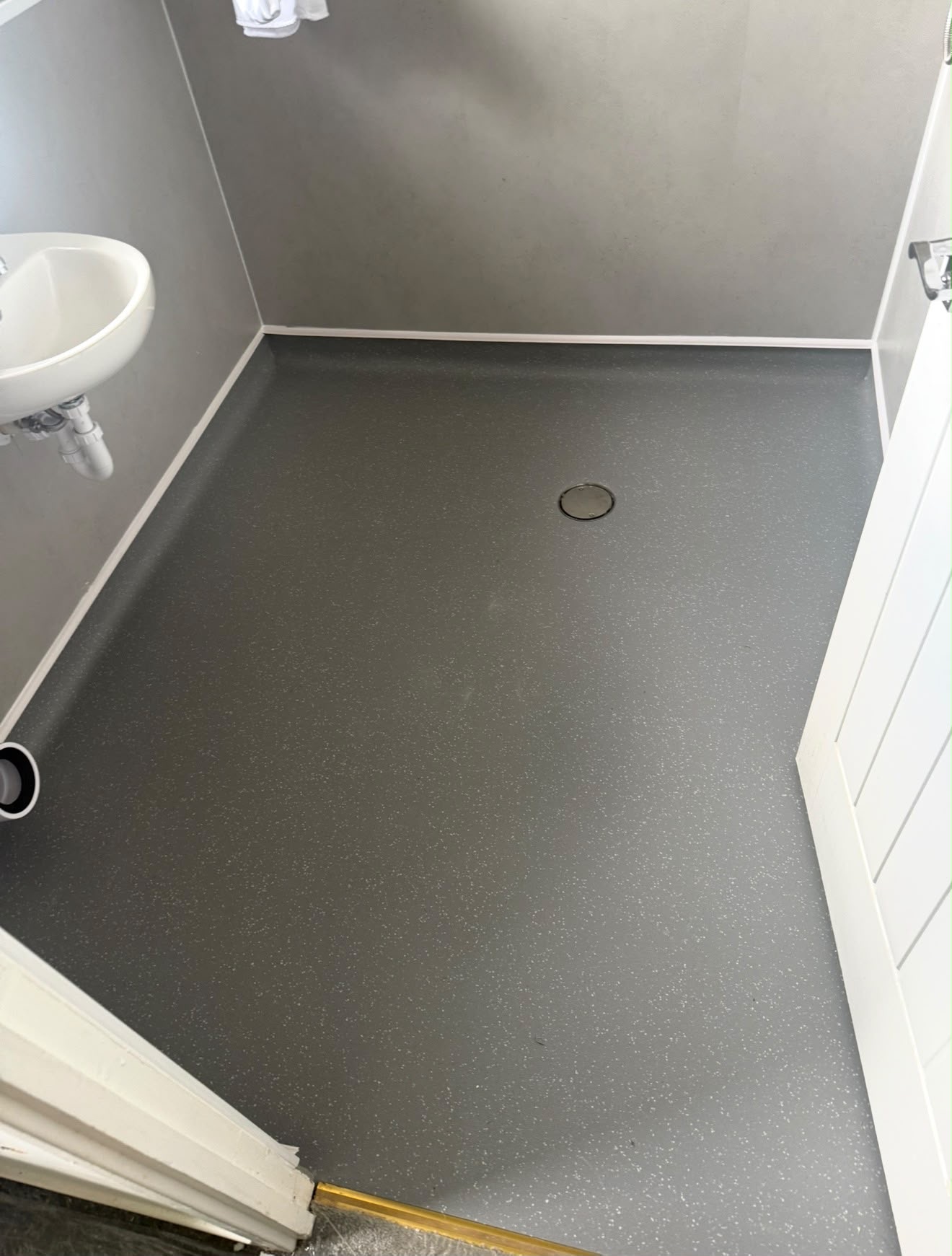 Grey speckled safety vinyl wet room floor with coved upstands and central drain