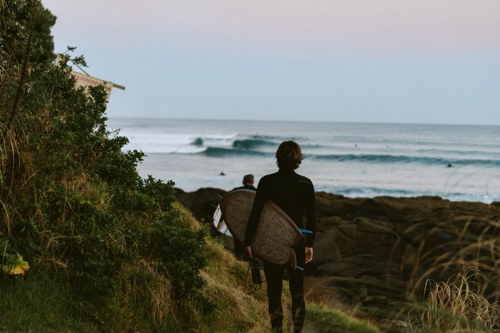 Surfers carrying boards along a coastal path at dusk in New Zealand