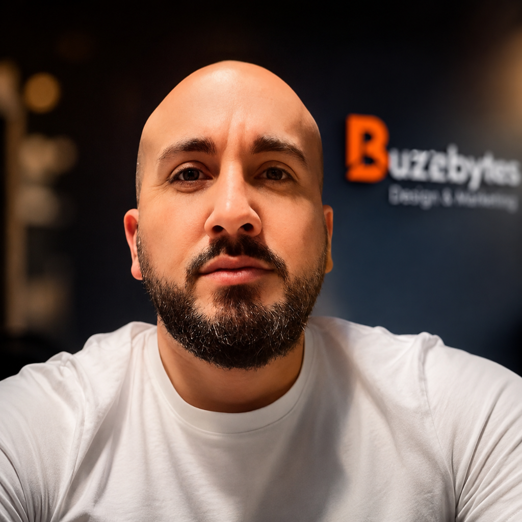 Darren Dudley, Founder and Director of BuzzBytes, wearing a white t-shirt in front of the BuzzBytes branded navy wall.