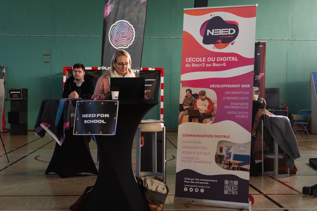 Une femme assise devant un ordinateur portable sur un stand d'entreprise avec un roll-up lors de LEVEL UP.