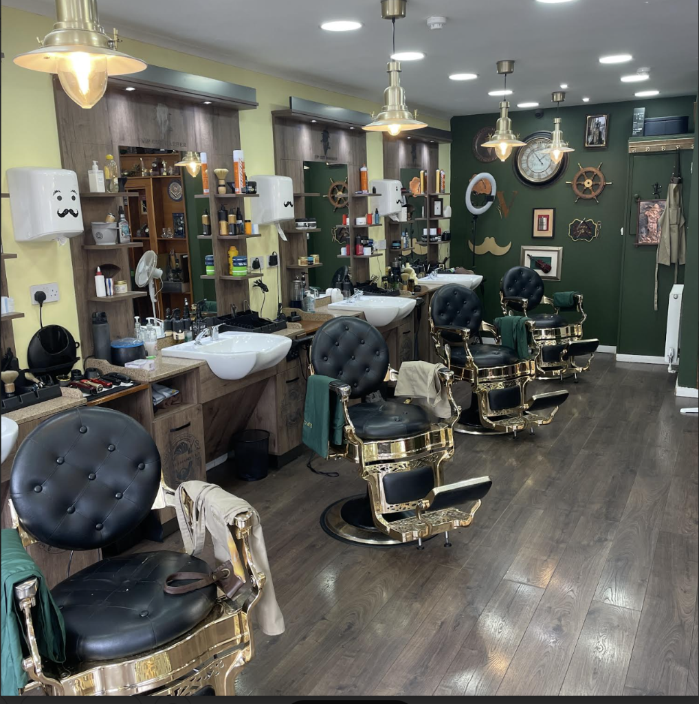 Wide interior view of VIP Cut Barber with gold-trim barber chairs, wood stations and olive green walls in Newton Mearns