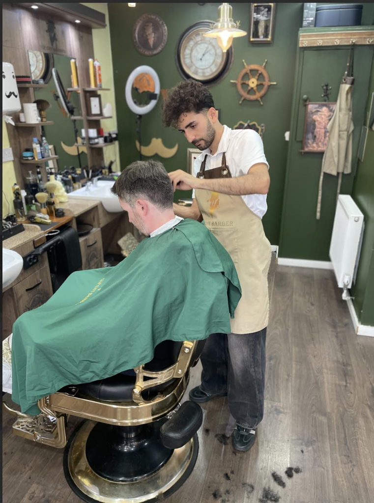 Barber cutting a client's hair at a wood-paneled VIP Cut Barber station with vintage decor