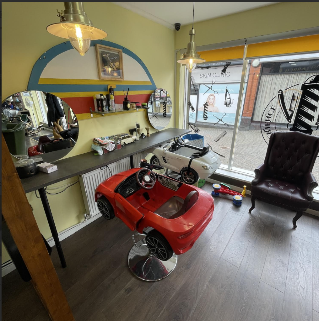 VIP Cut Barber interior featuring red and white children's car chairs and tufted leather armchair