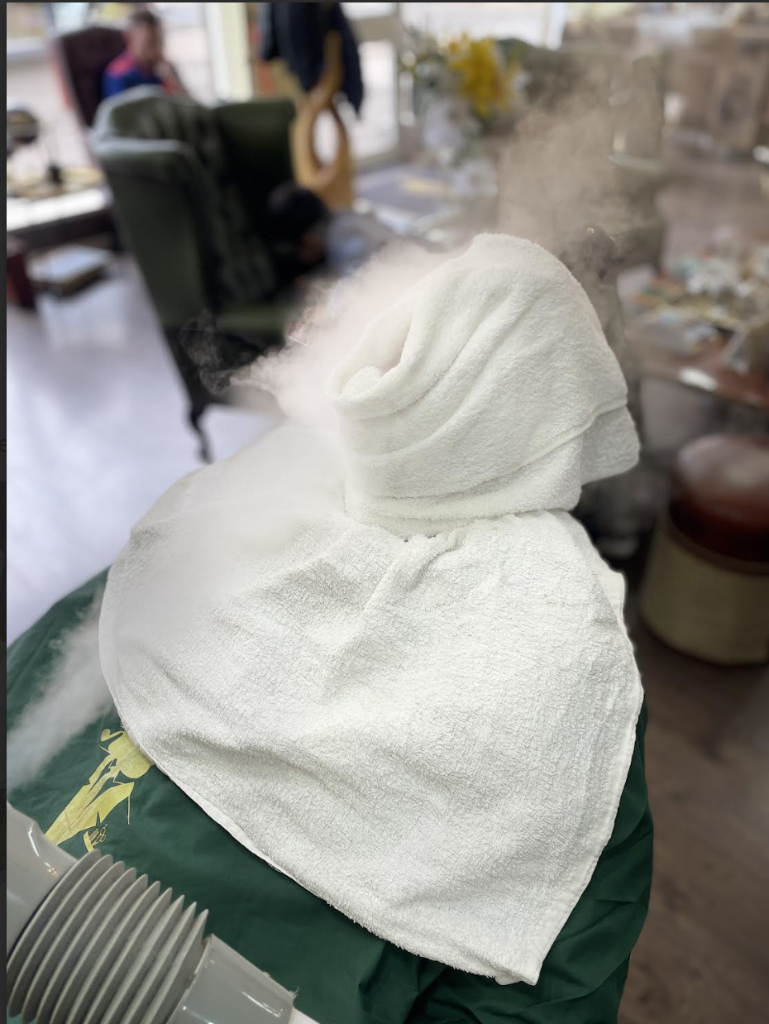 Hot towel treatment with rising steam during a traditional shave at VIP Cut Barber