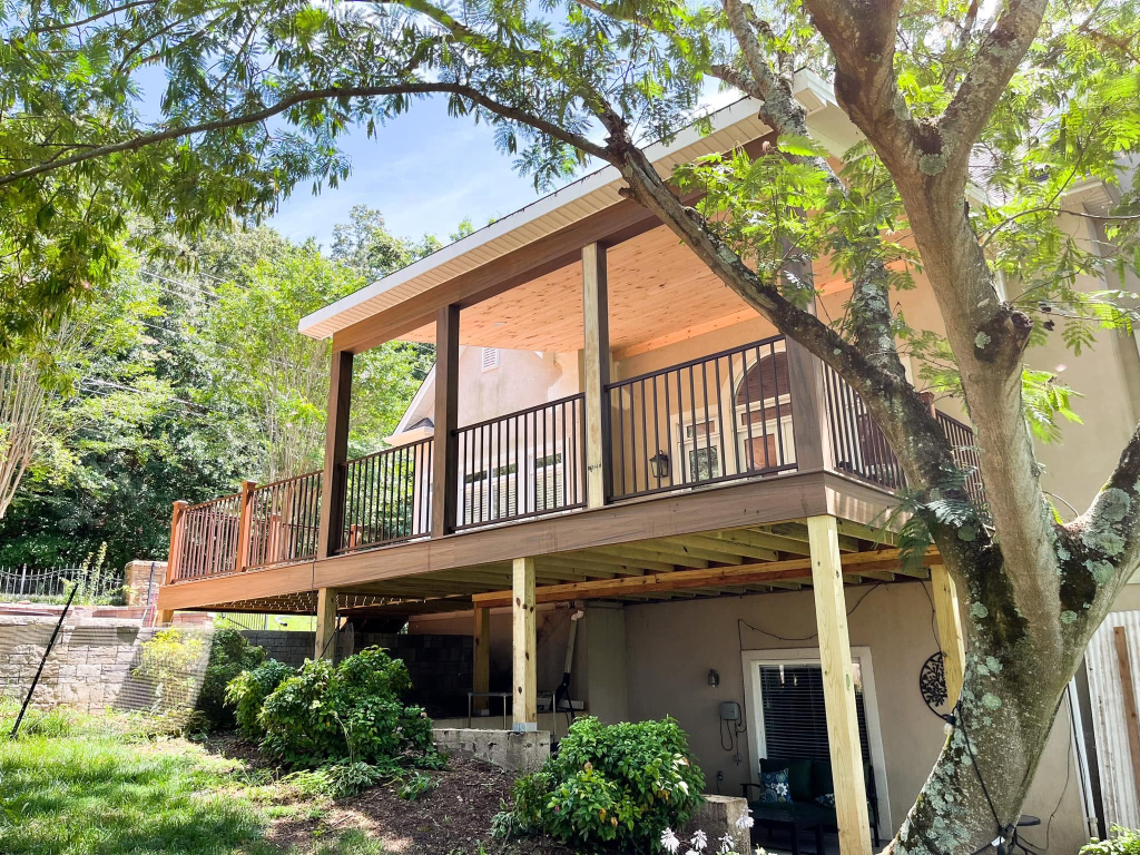 Newly constructed elevated wooden deck with tongue-and-groove ceiling, black metal railing, and lush wooded backdrop