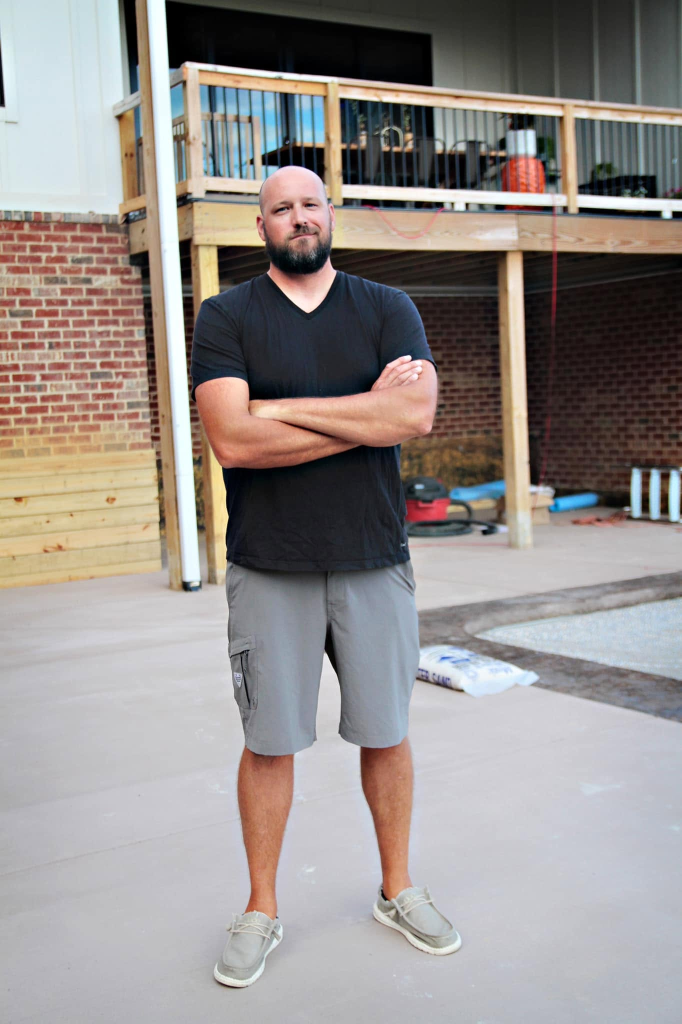 Matt Newland, owner of Newland Construction, on a job site standing on a newly poured concrete patio in front of a home under construction