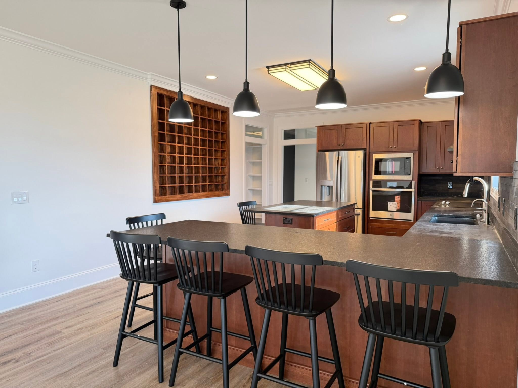 Contemporary L-shaped kitchen with dark-stained cabinets, charcoal stone countertops, black bar stools, and matte pendant lights