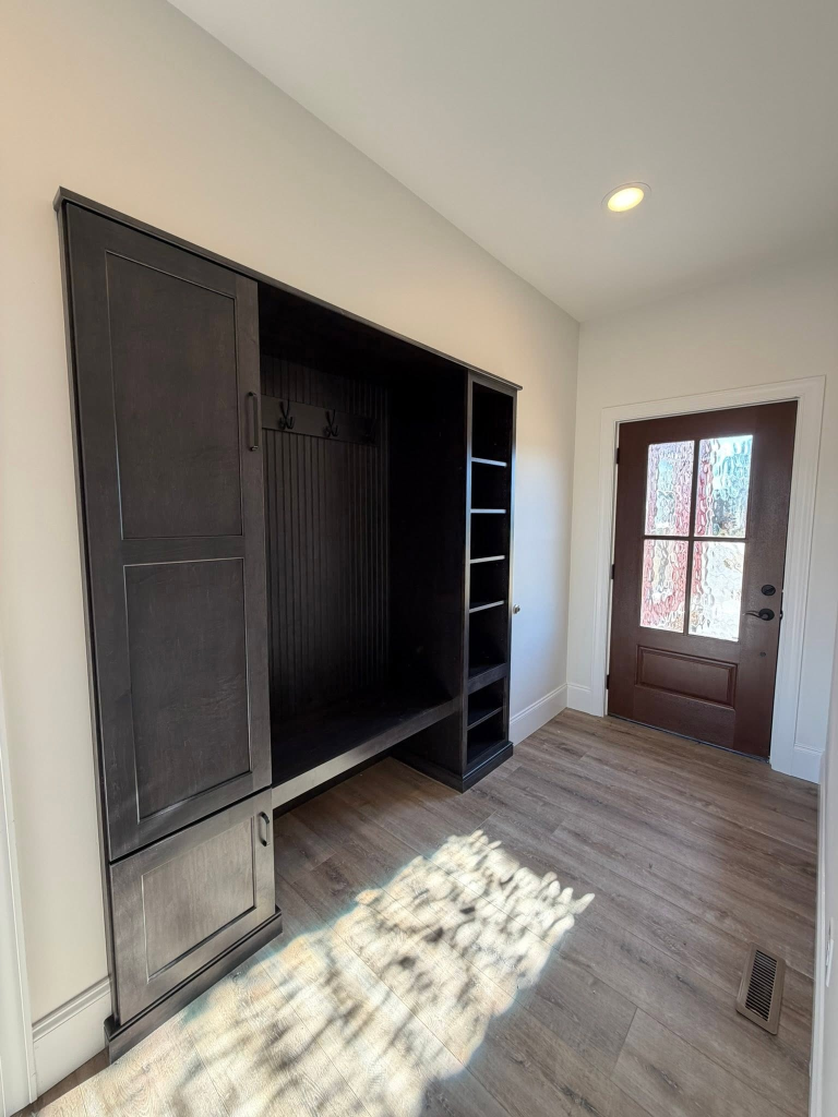 Custom mudroom built-in with dark wood storage unit, bench with coat hooks, cubby shelving, and a glass-paneled exterior door