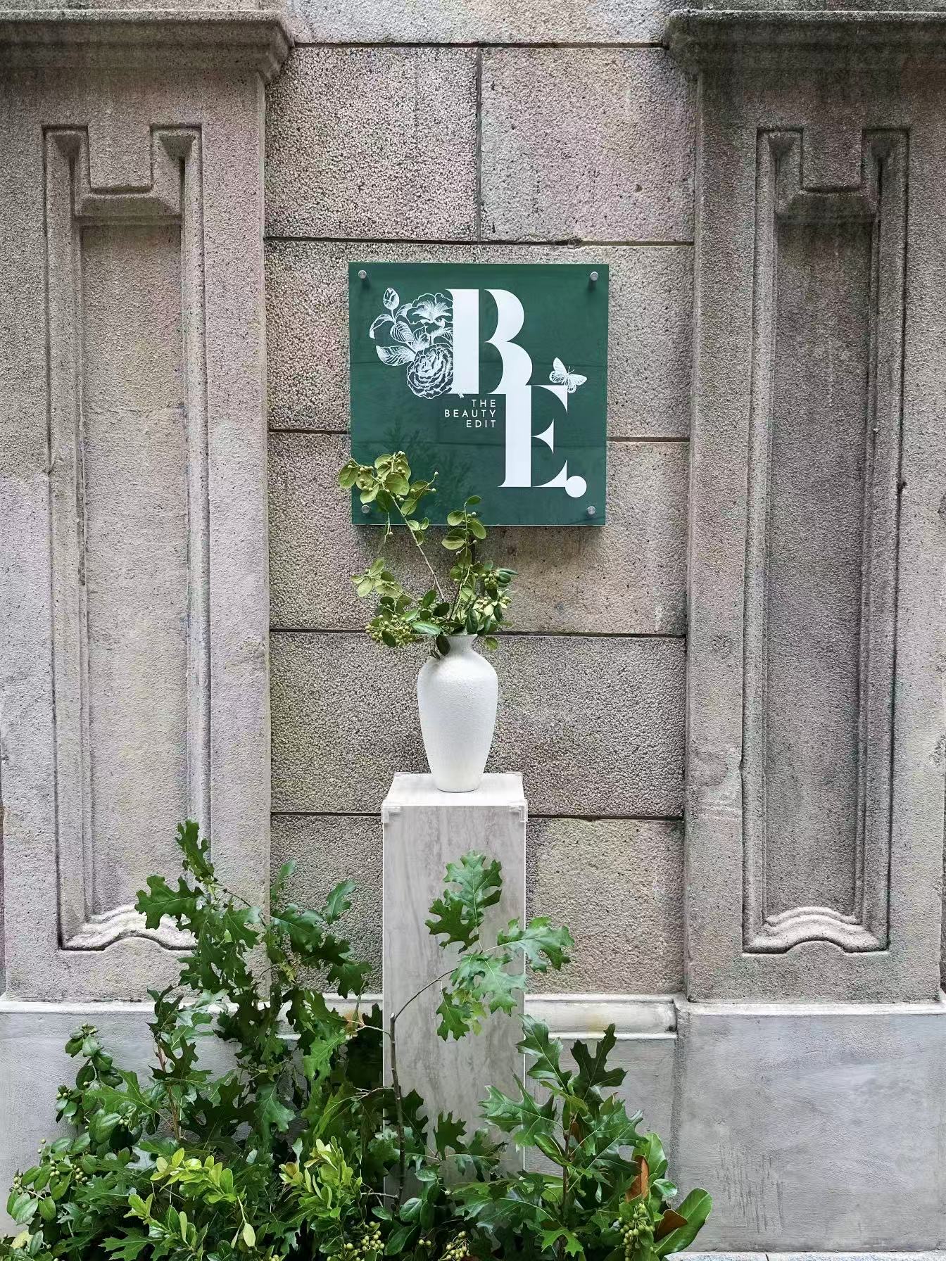 The Beauty Edit plaque mounted on the stone facade, with a vase of foliage below
