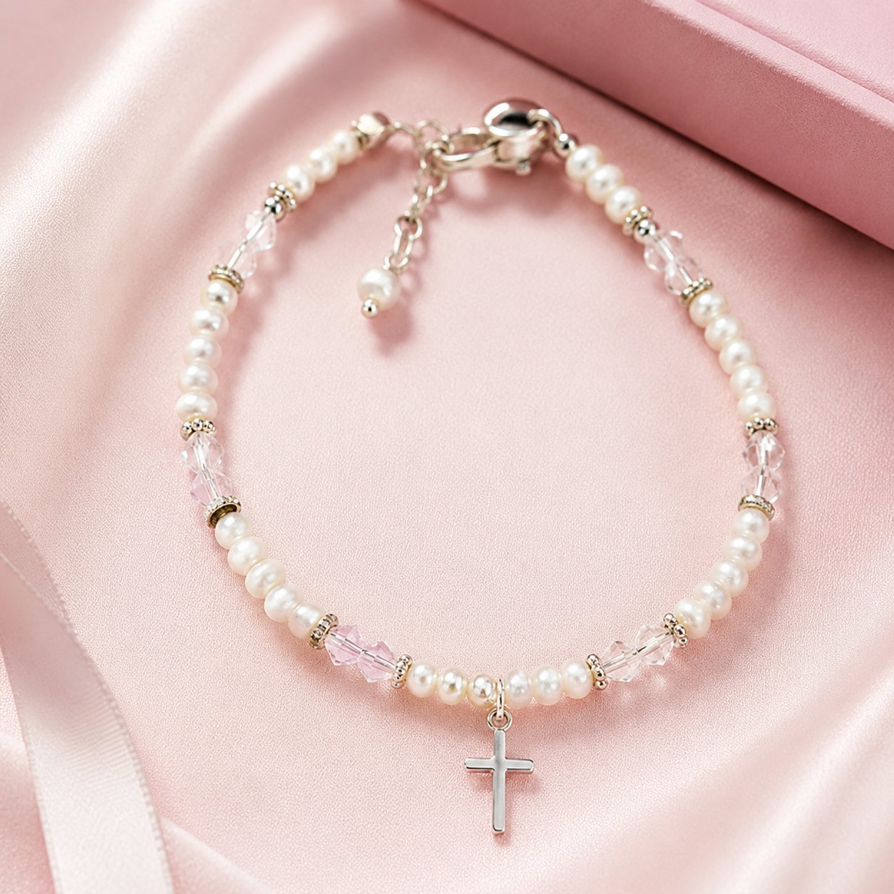 Pearl bracelet with clear and pink crystal accents and a silver cross charm on pink satin