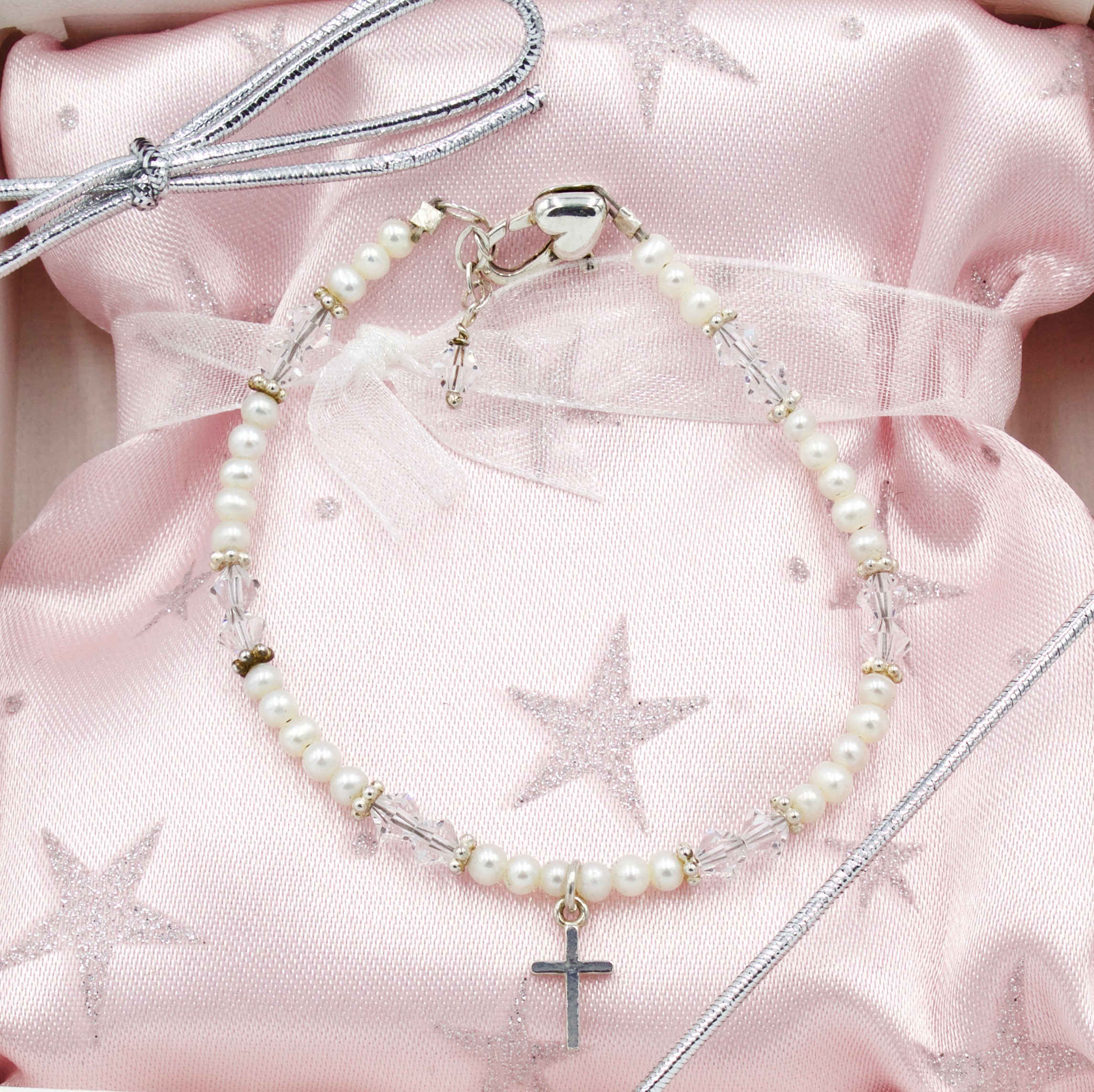 Delicate pearl and crystal bracelet with cross charm presented on pink satin.