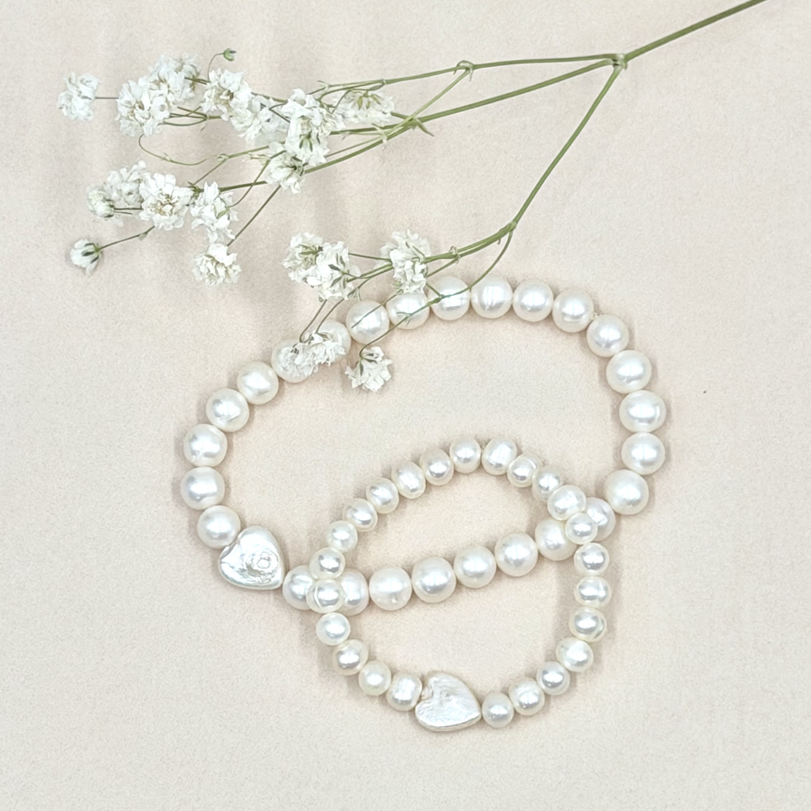 Two pearl bracelets with silver heart charms arranged with baby's breath on linen