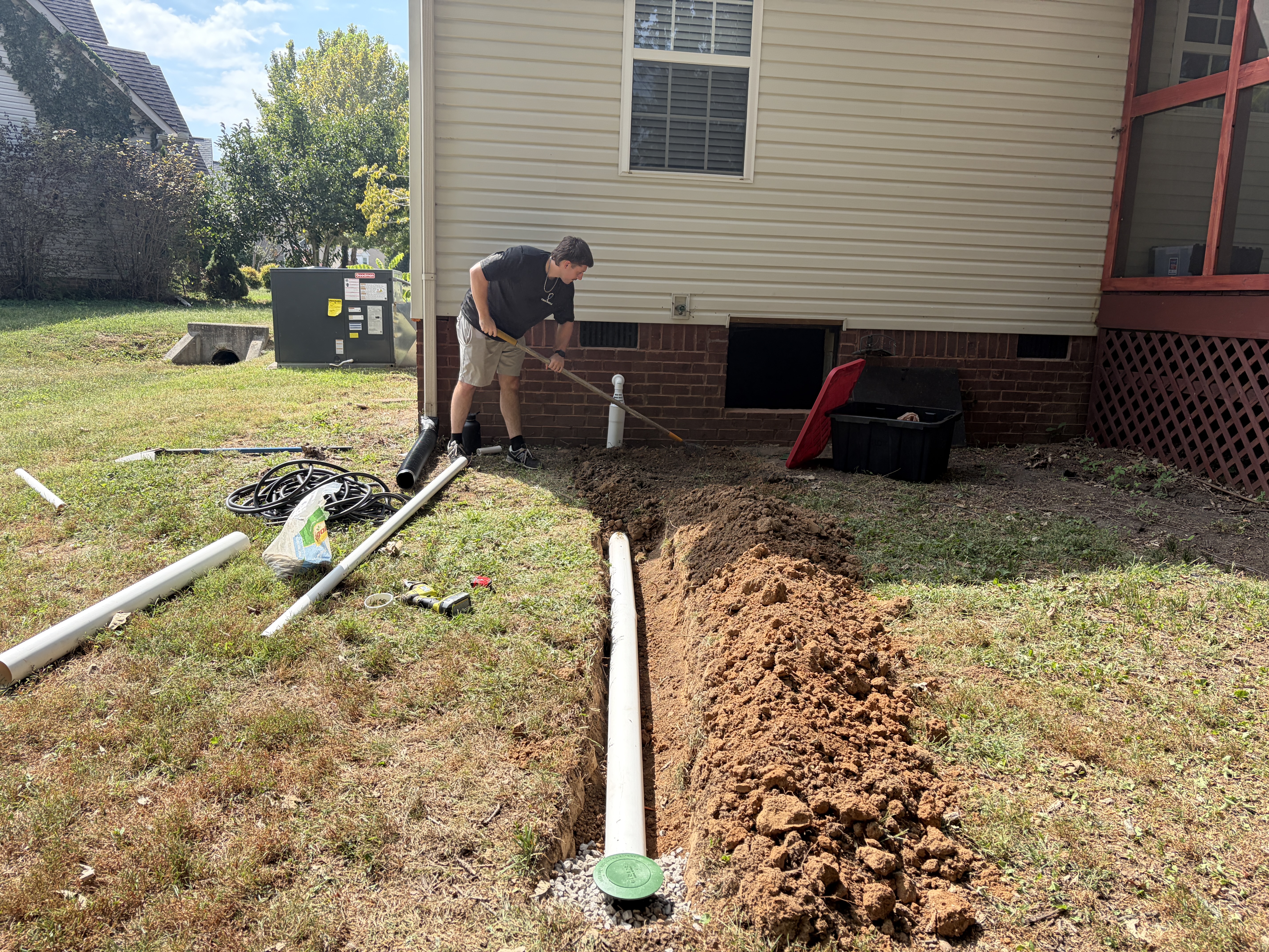 Crawl space drainage installation with a PVC discharge pipe routed through an exterior trench to a drainage grate away from the foundation of a Murfreesboro, TN home by The Crawl Shield