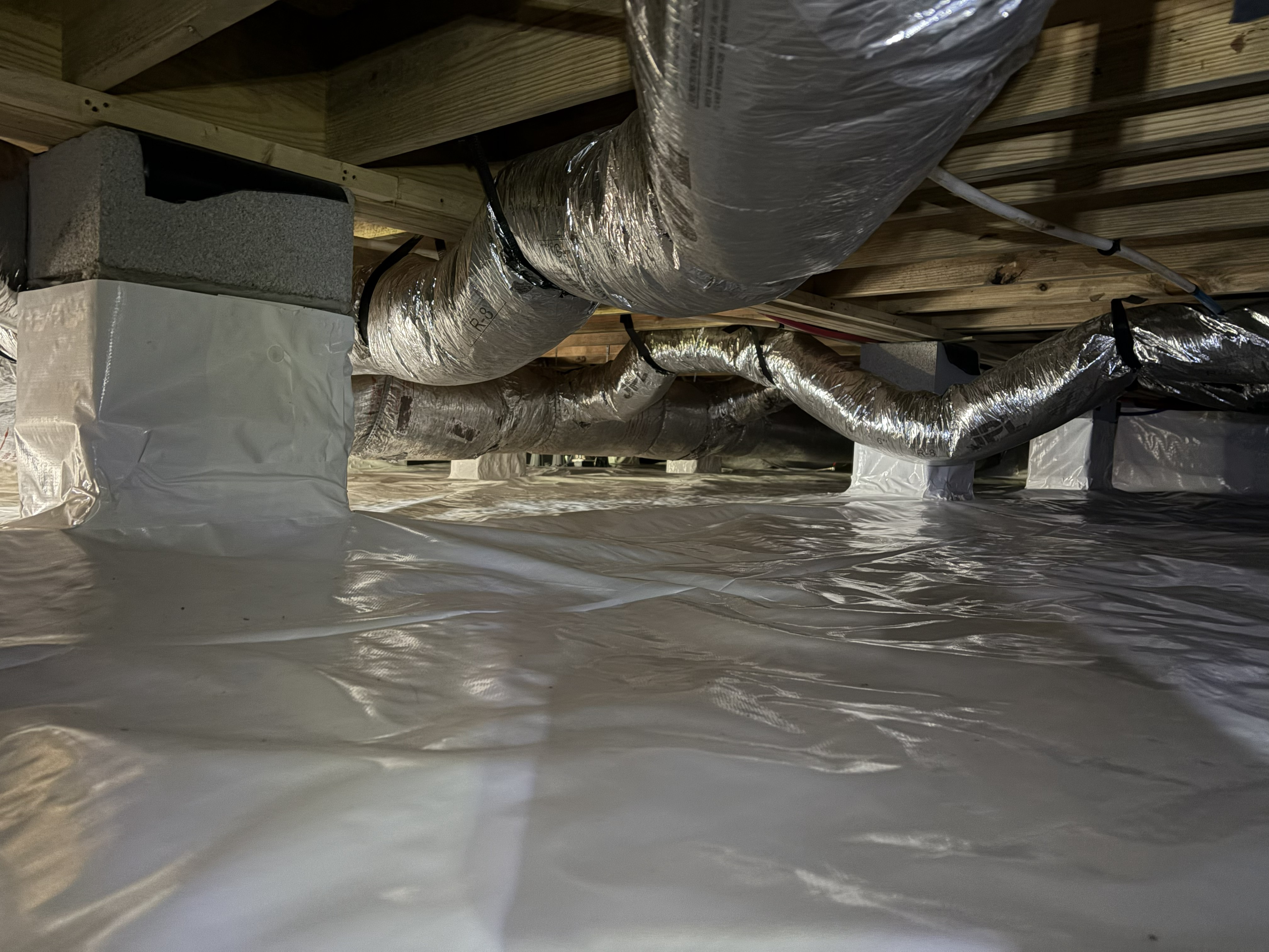 Insulated HVAC ductwork and a white vapor barrier in a professionally maintained encapsulated crawl space