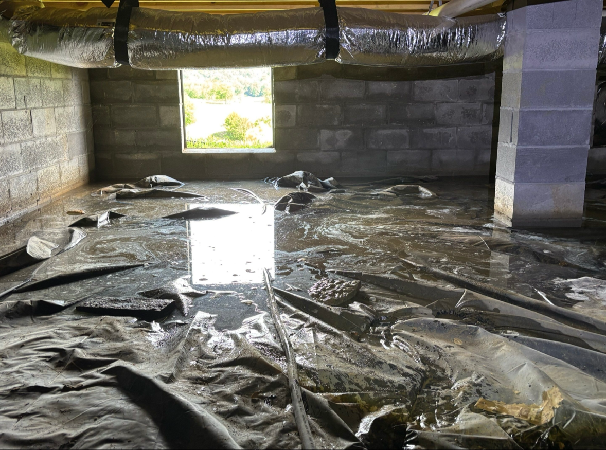 Standing water in a Murfreesboro, TN crawl space before water mitigation, showing a black vapor barrier over saturated ground and a foundation vent