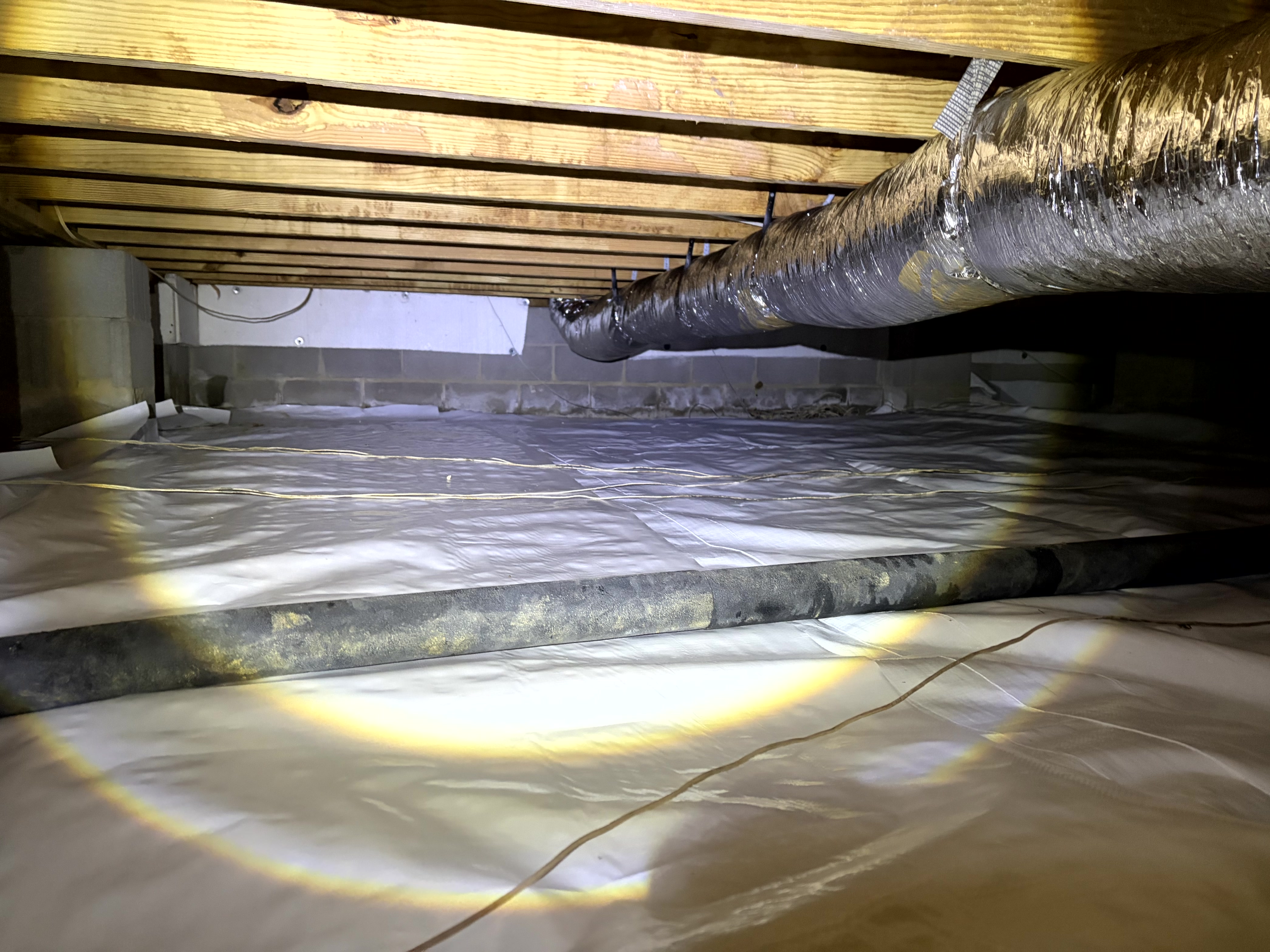 White reinforced crawl space vapor barrier installed across the floor with sealed insulated HVAC ductwork and a drainage pipe in a Murfreesboro, TN home by The Crawl Shield