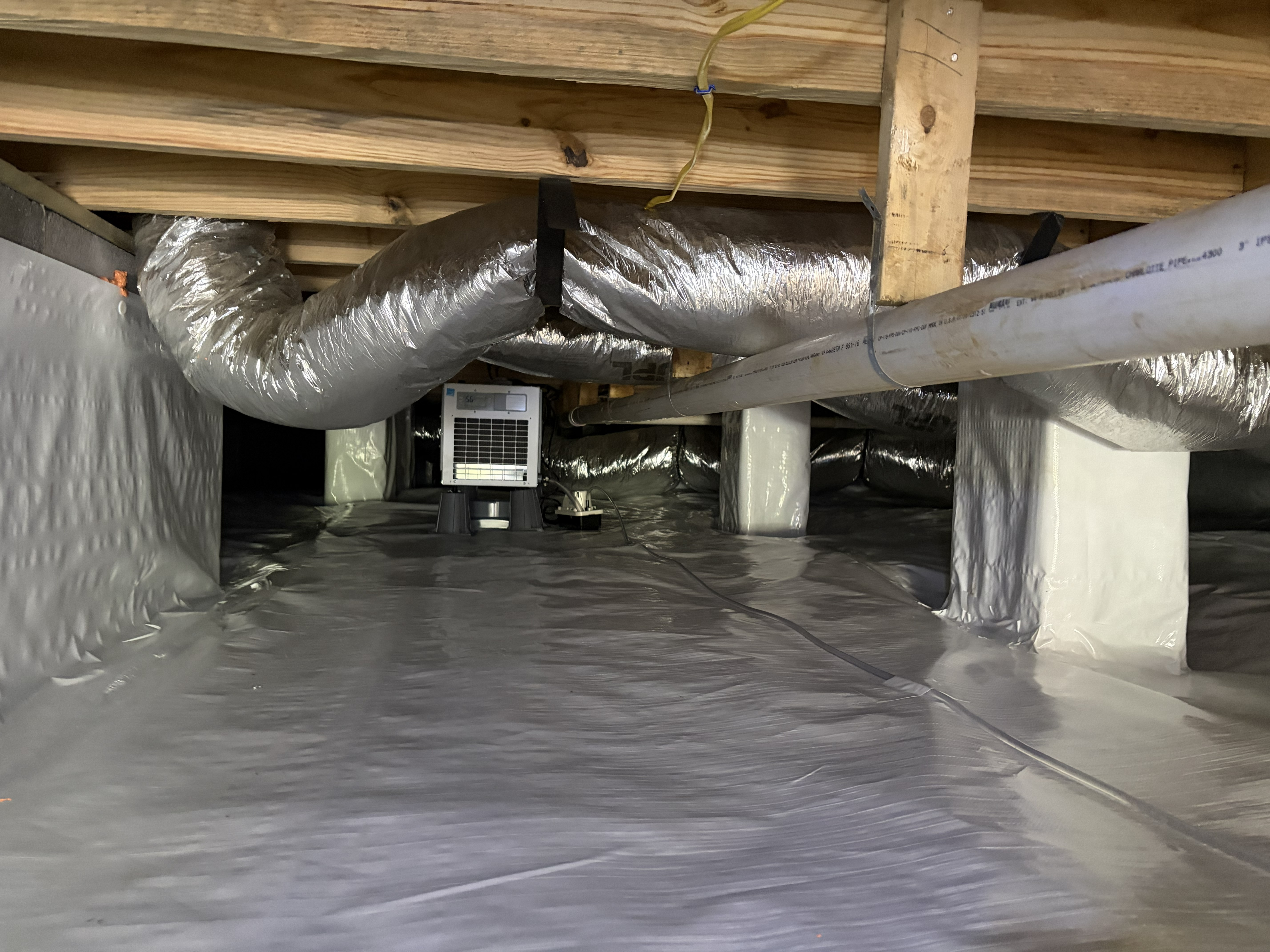 Crawl space dehumidifier and PVC drainage installed over a white vapor barrier during encapsulation in Murfreesboro, TN