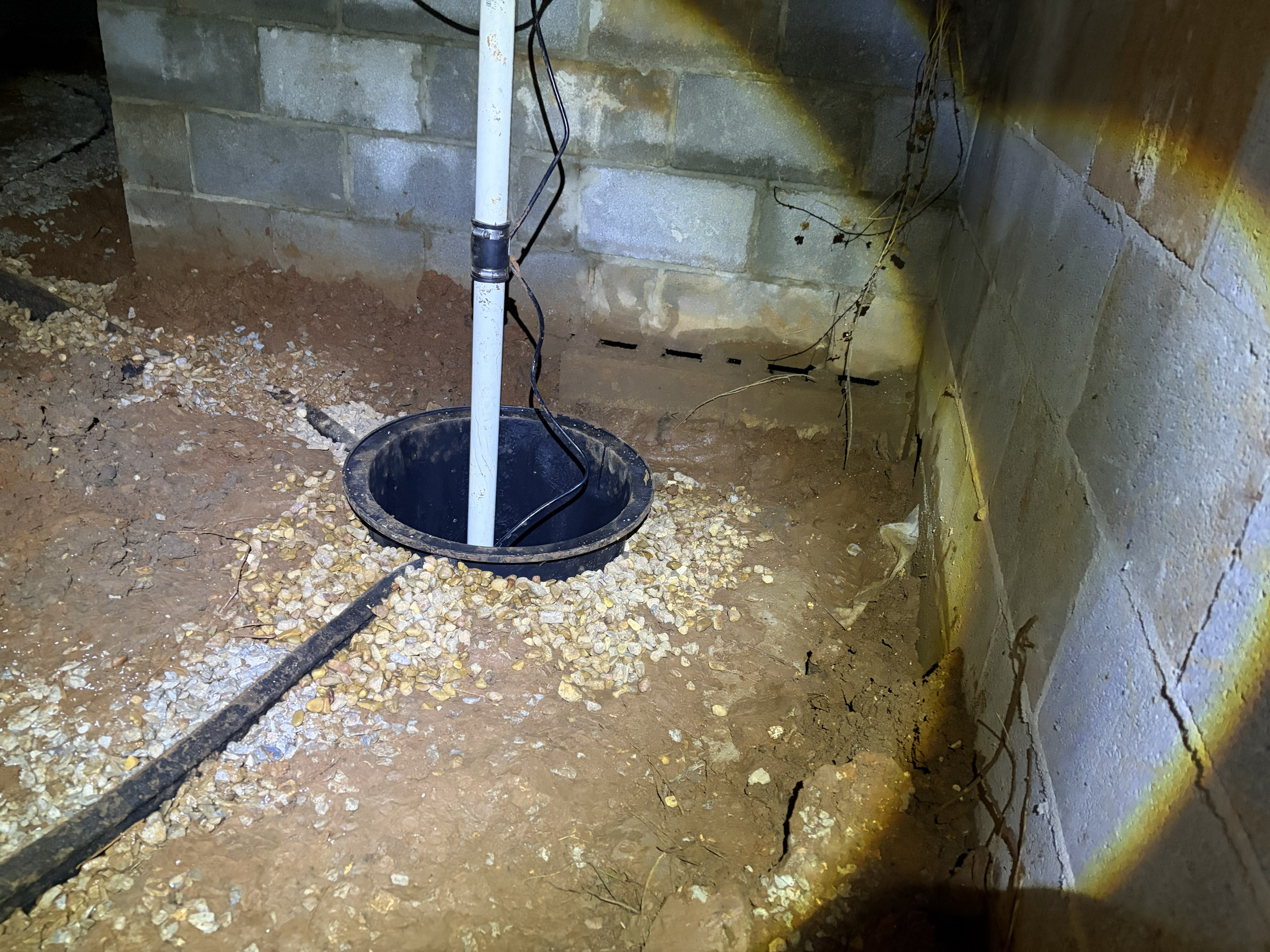 Newly installed sump pump basin set in gravel for crawl space water mitigation in a Murfreesboro, TN home