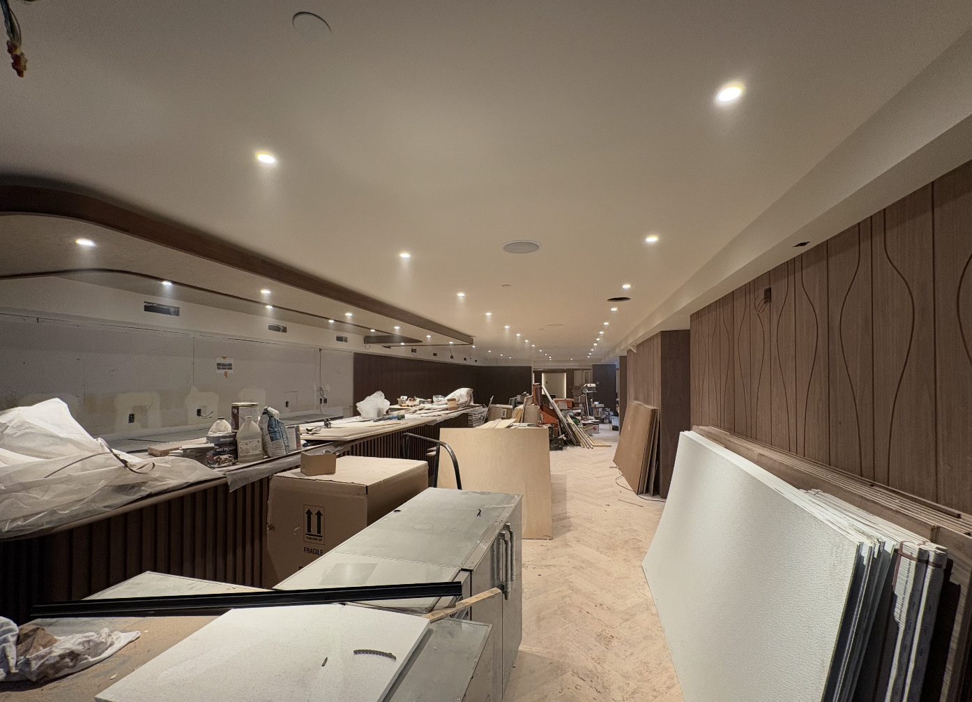 Second Seafire Grill location under construction with sculpted walnut wall panels, a long slatted wood bar, curved soffit lighting and herringbone subfloor