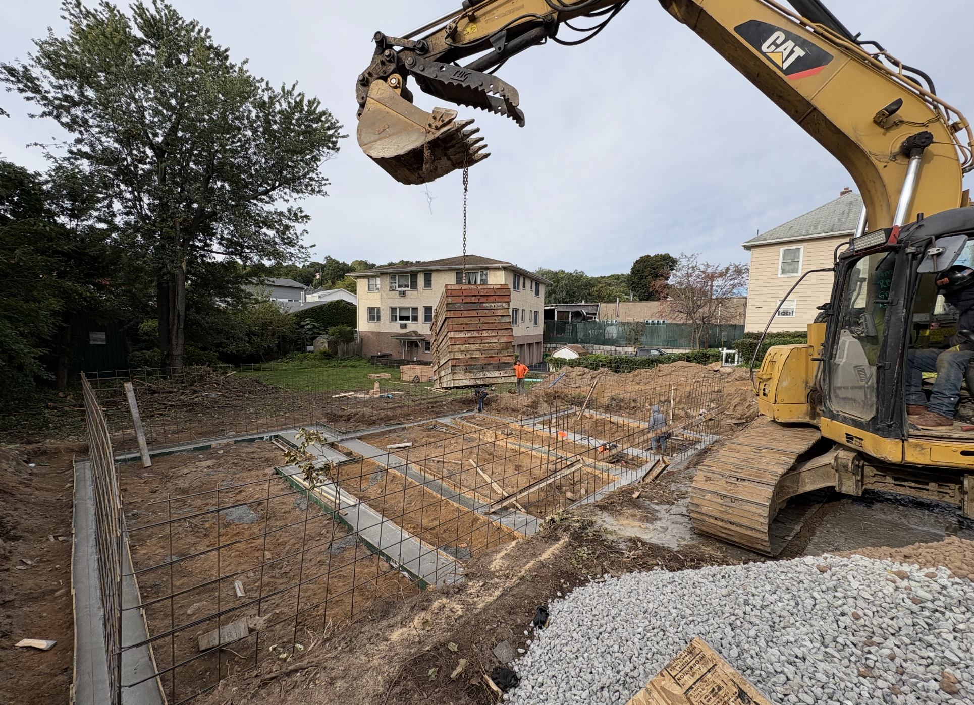 Excavator lowering concrete forms into a freshly dug foundation with poured footings and rebar in Nyack, NY