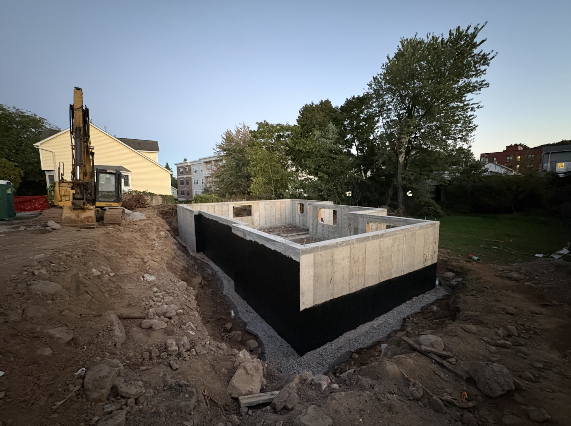 Poured concrete foundation with black waterproofing membrane and gravel drainage for a new build in Nyack, NY, with an excavator on site