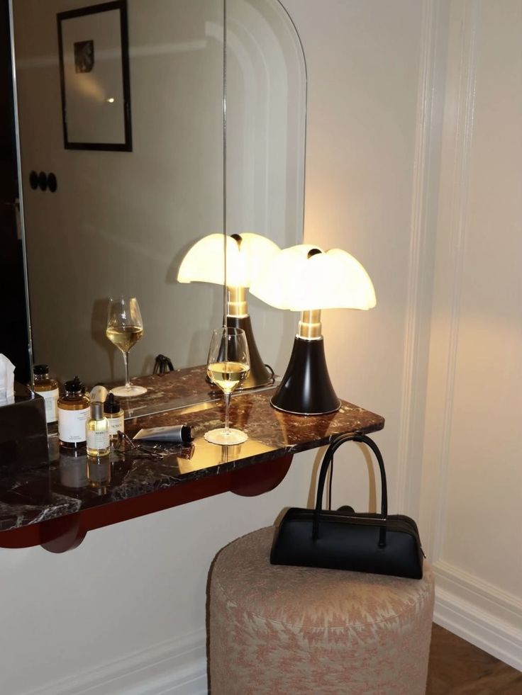 Coiffeuse en marbre noir veiné, lampe Pipistrello, miroir cintré et sac noir sur pouf