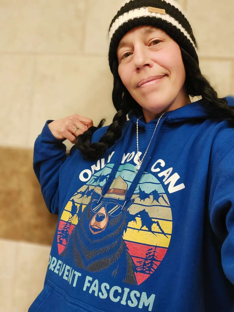 Crystal Butcher wearing a beanie and a blue hoodie with a Prevent Fascism graphic print