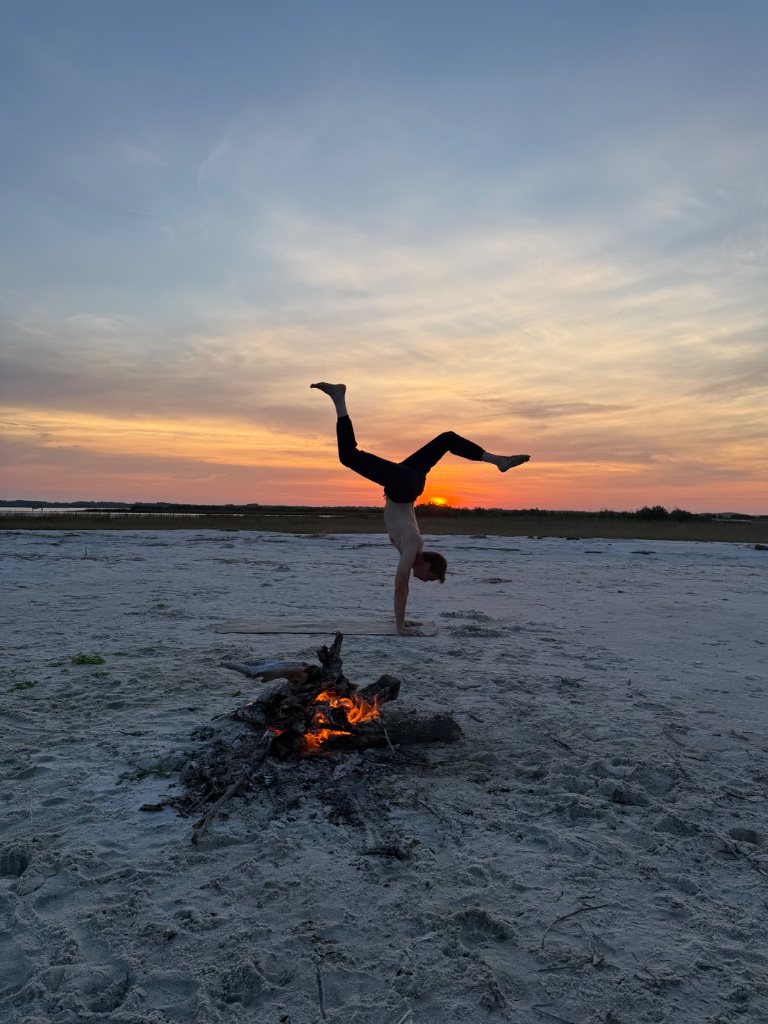 Matthew Shield performing a handstand on the beach at sunset