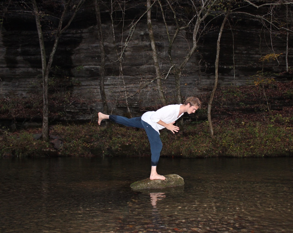 Matthew Shield in a Warrior III balance on a stream rock