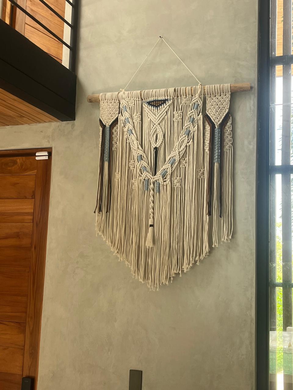 Macramé wall hanging with dusty blue and dark brown accents on driftwood