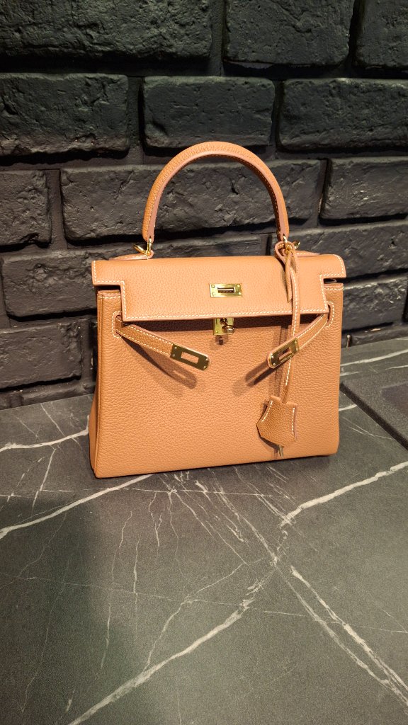 Front view of Hermès Kelly bag in Togo leather, gold-brown color, on marble surface