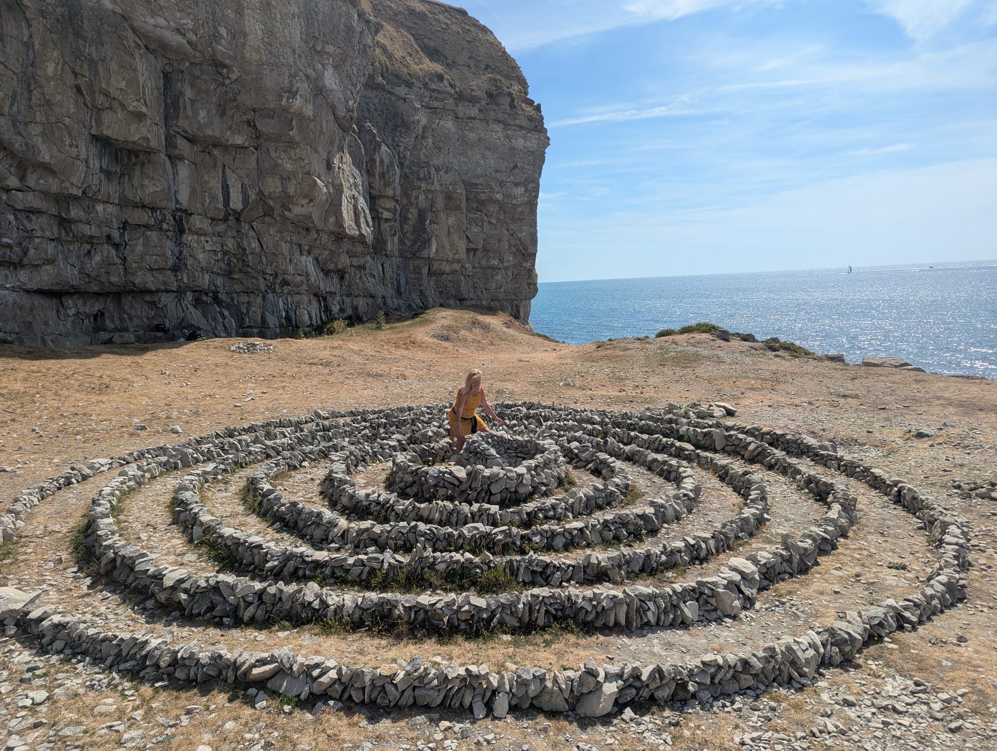 A stone Global Spiral™ beside a limestone cliff above the sea
