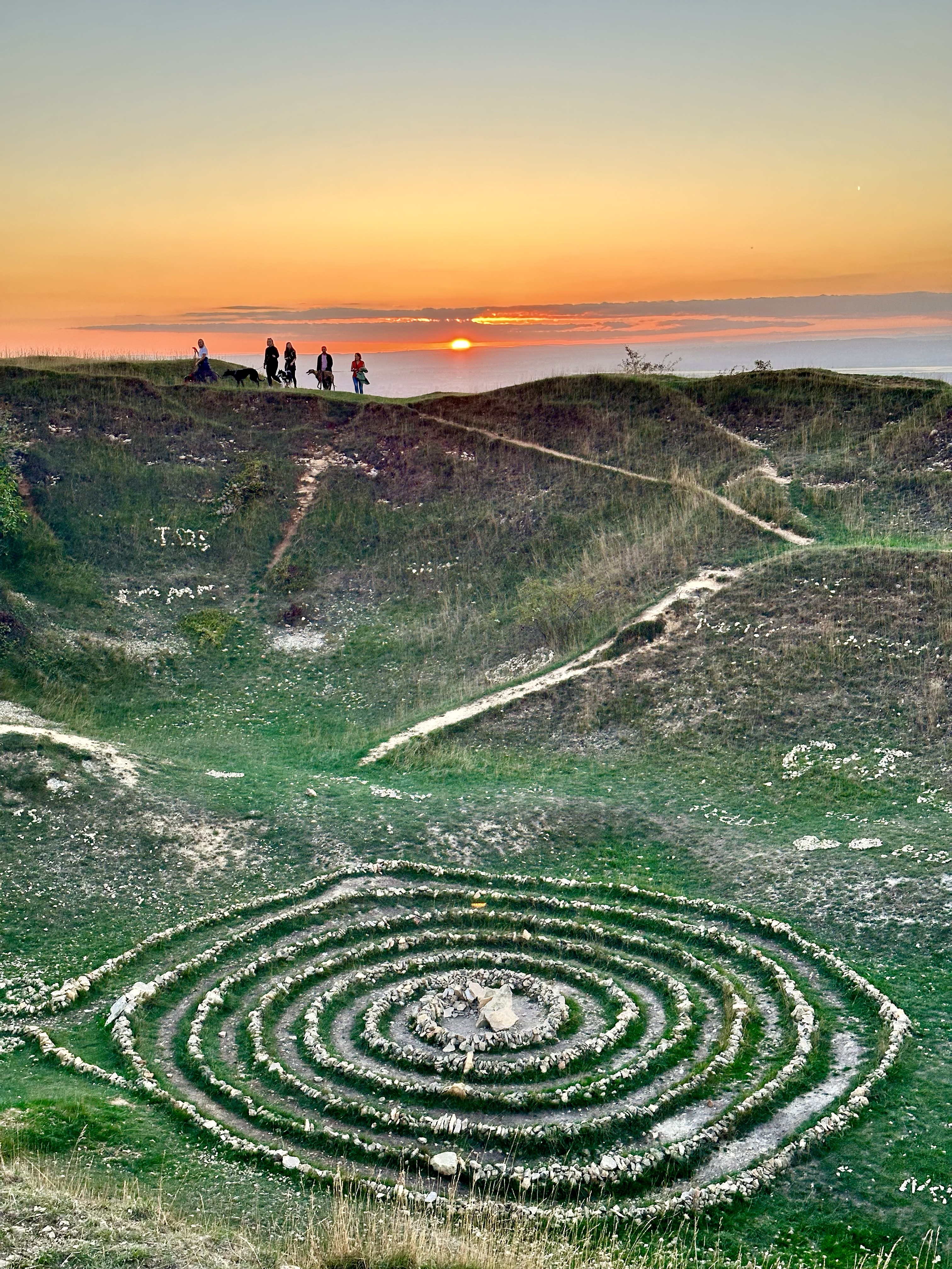 A stone spiral below a ridge of walkers at sunset