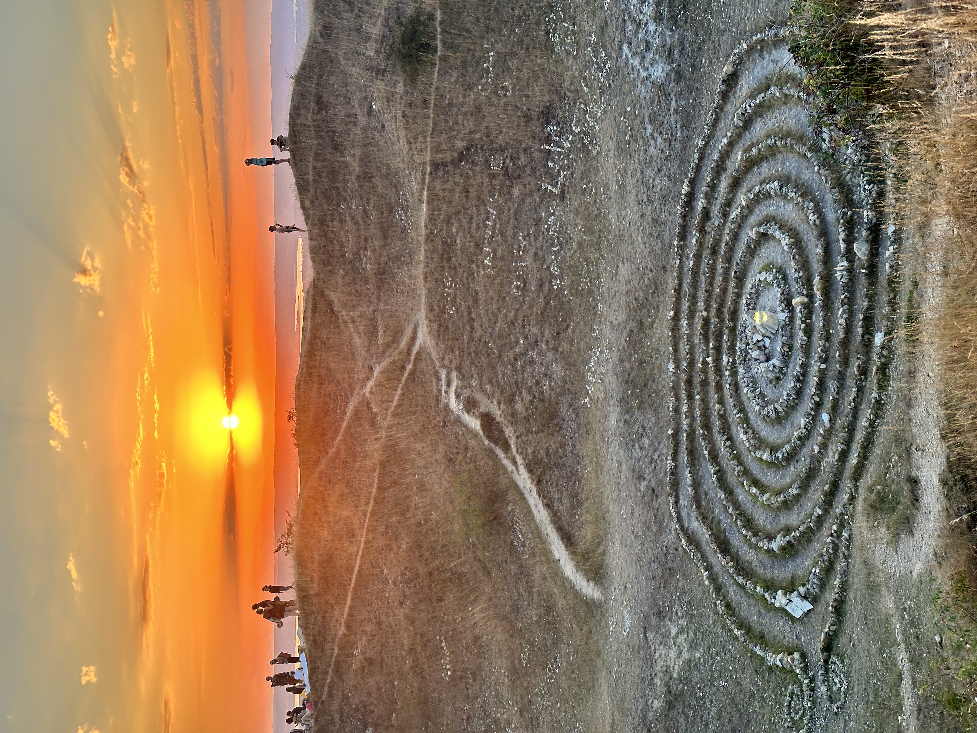 A stone Global Spiral™ on a hillside beneath an orange sunset