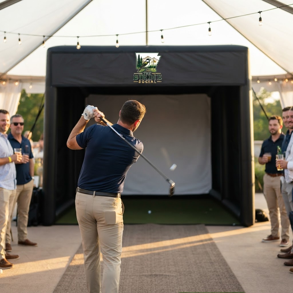 Birdie Social branded matte black inflatable golf simulator enclosure set up at a twilight outdoor event with guests, balloons, and golf bags