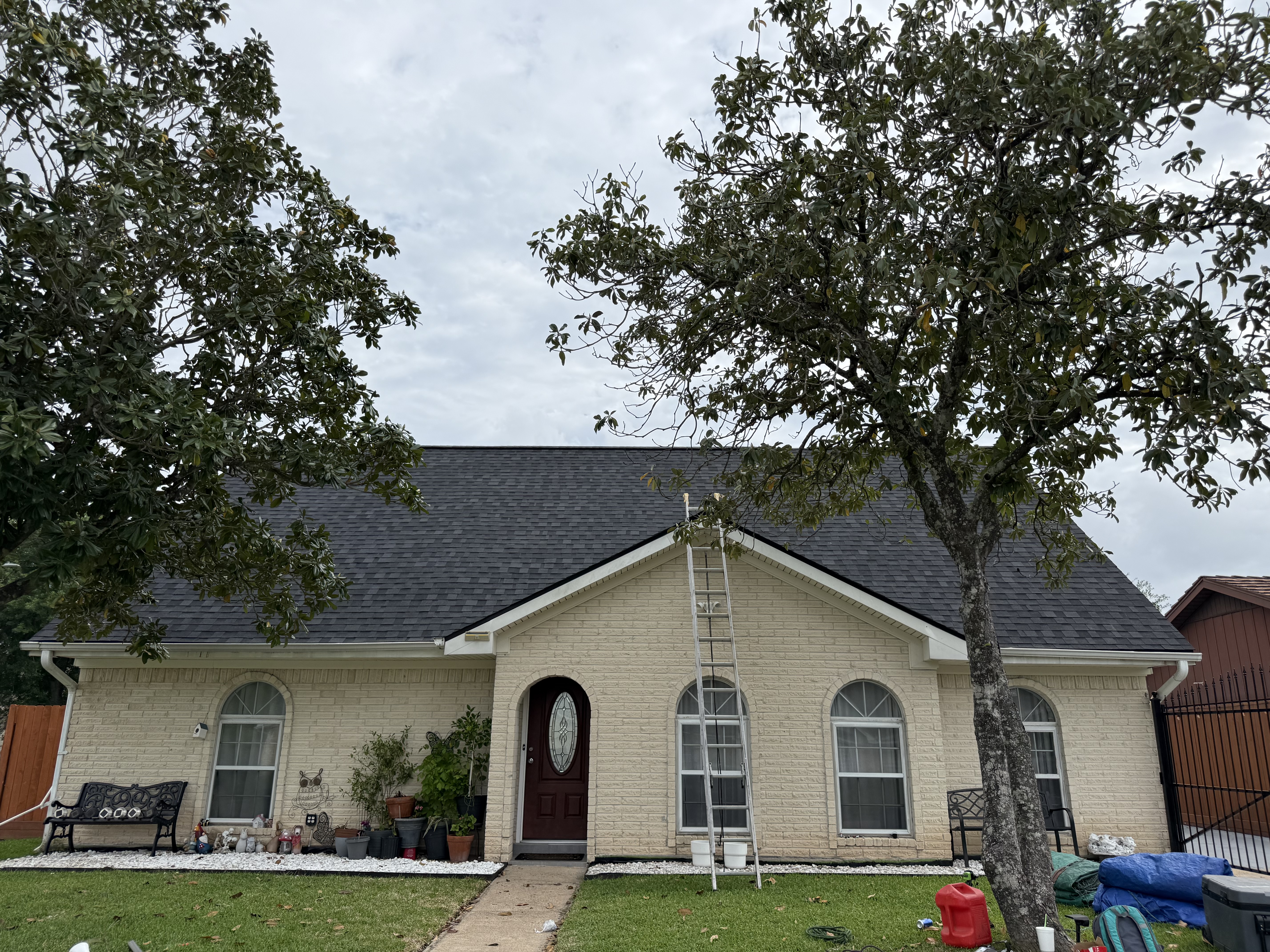Completed dark asphalt shingle roof on a cream brick Houston home